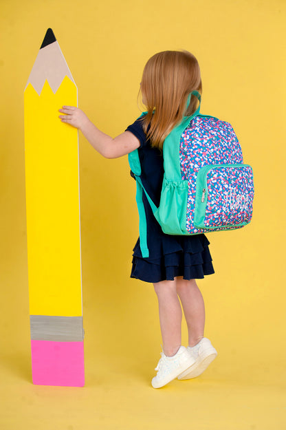 Child wearing a confetti-print preschool backpack beside a giant pencil prop