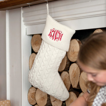 Cream cable knit Christmas stocking with red monogram hanging from a mantel
