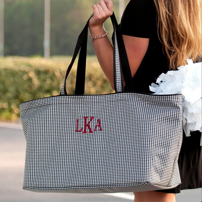 Gray houndstooth tote with red initials carried by its handles