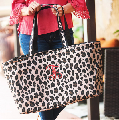 Tan leopard-print tote with a red monogram carried by hand
