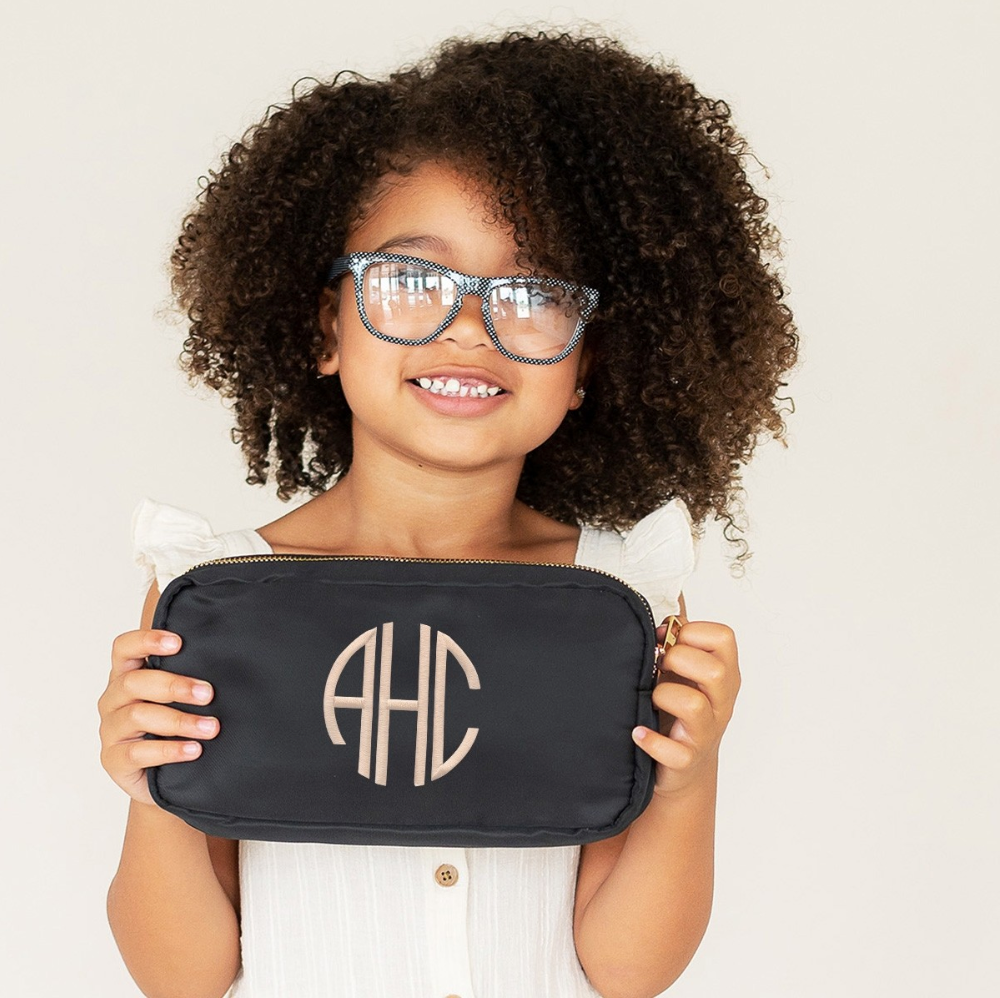 Child holding a black accessory pouch with a cream monogram