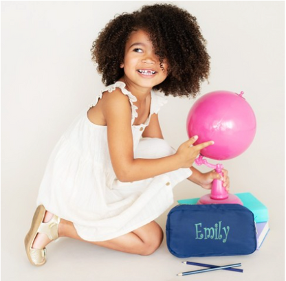Child seated beside a navy pouch embroidered with Emily