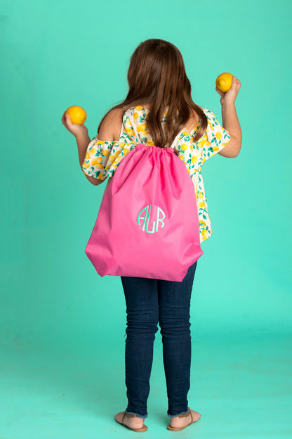 Child wearing a pink drawstring bag with a monogram