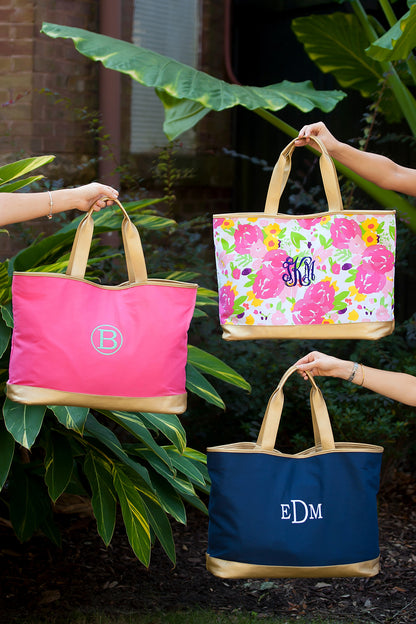 Pink, floral and navy personalized totes with gold-colored trim arranged among leaves