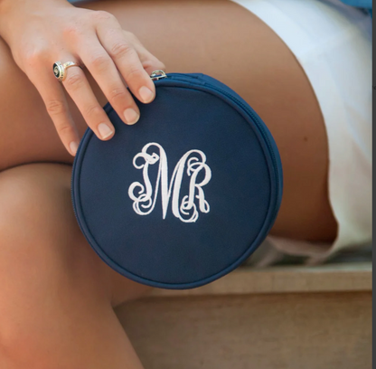 Navy round jewelry case with a white monogram held on a lap