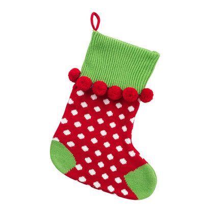 Red dotted knit stocking with green cuff, heel and toe and red pom-poms on white